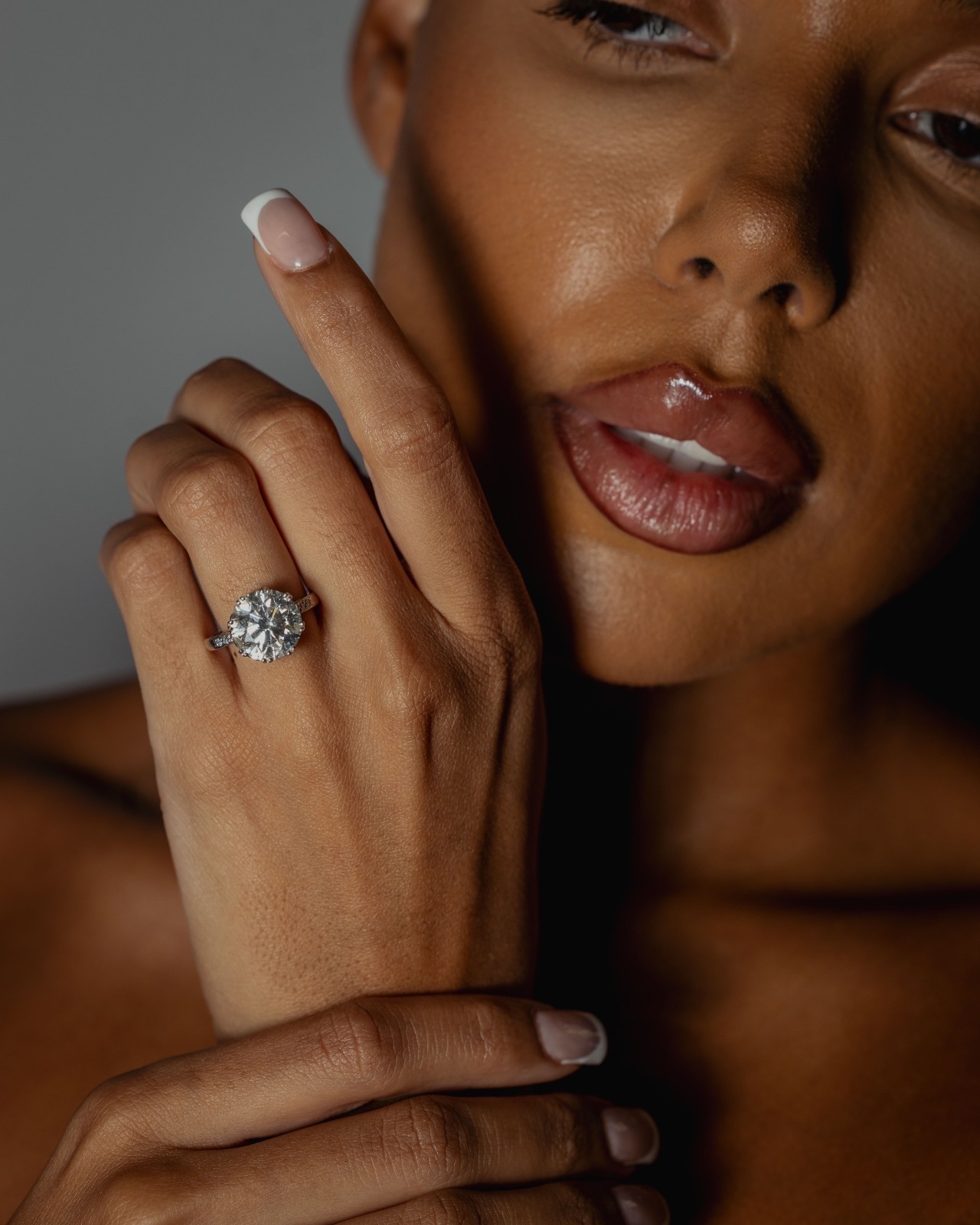 A round brilliant diamond solitaire ring with diamond-set shoulders, worn on the hand