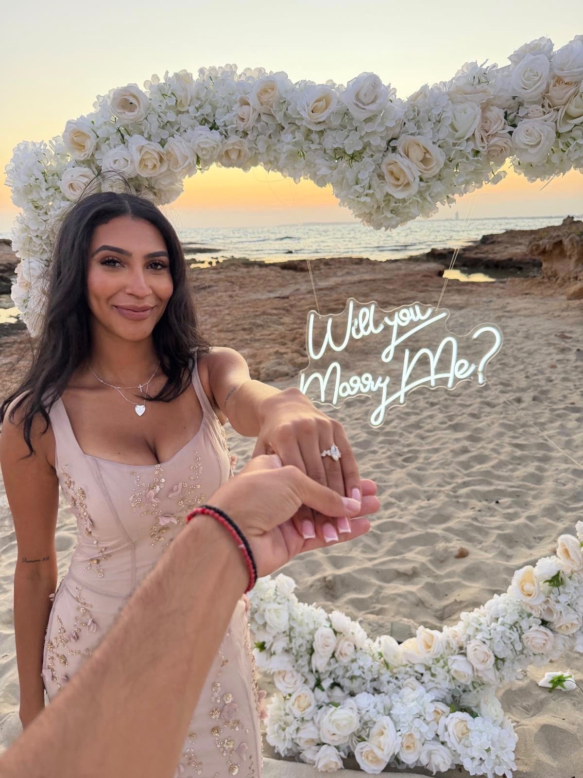A proposal on the beach at sunset, the engagement ring held up to the camera
